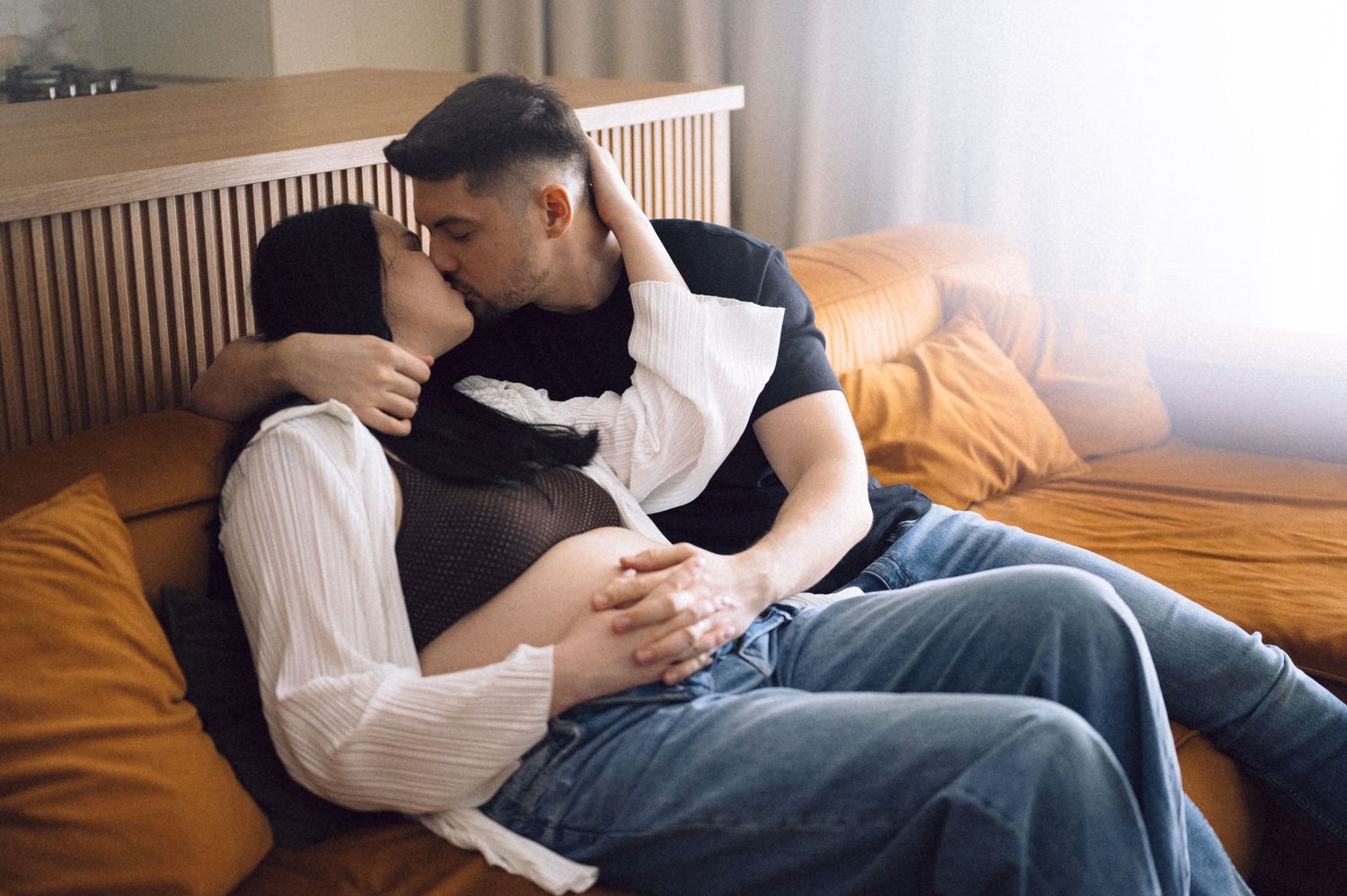 Couple in casual clothing sharing an intimate moment while relaxing together on a brown couch.