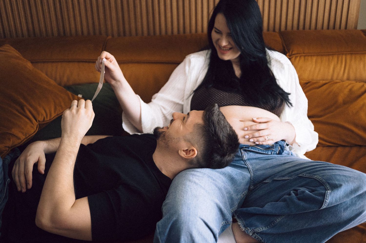 A couple relaxes together on a brown leather couch, sharing an intimate moment in casual attire.