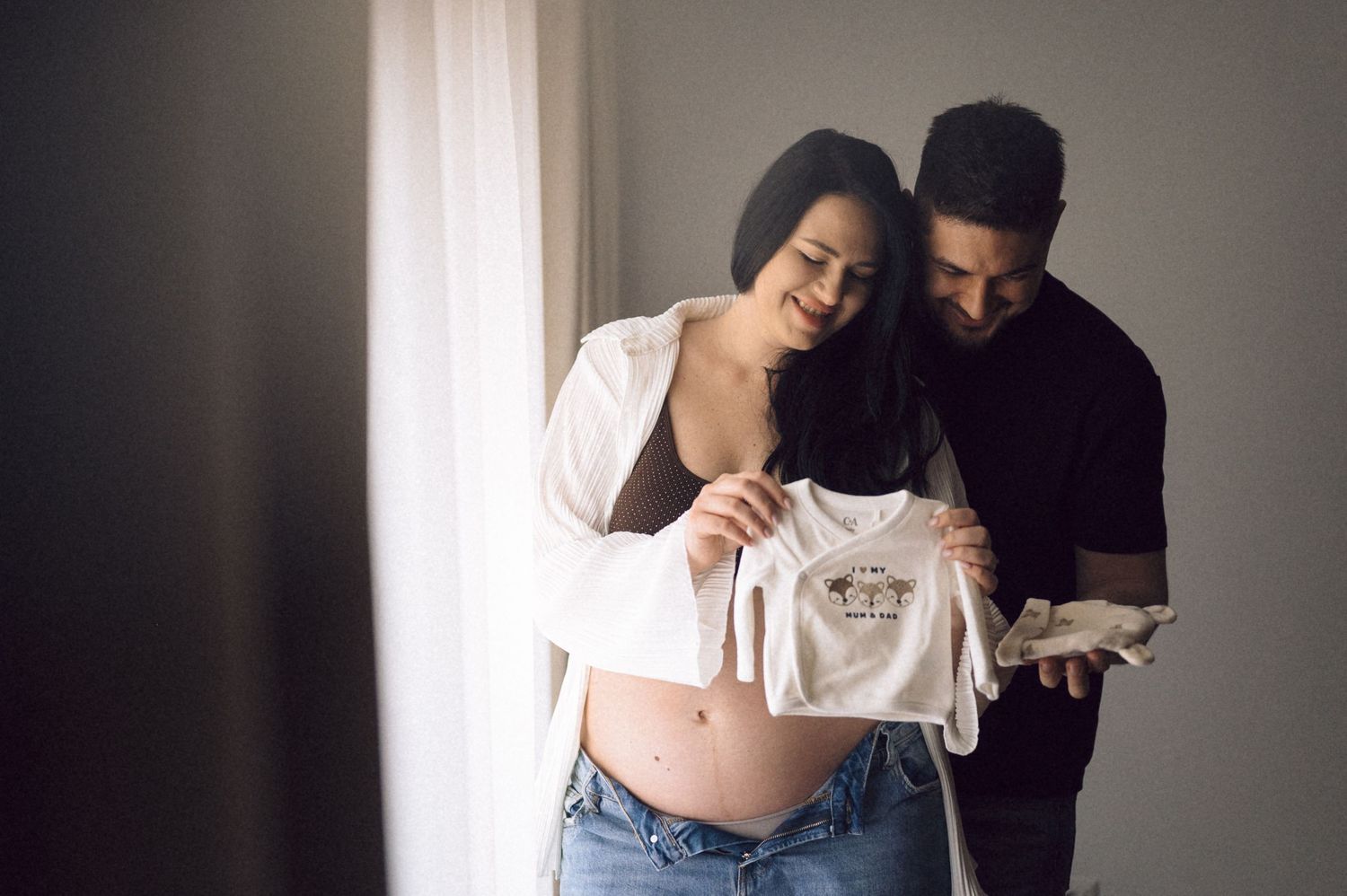 Intimate maternity photo series showing a couple embracing in soft natural light against a neutral wall.