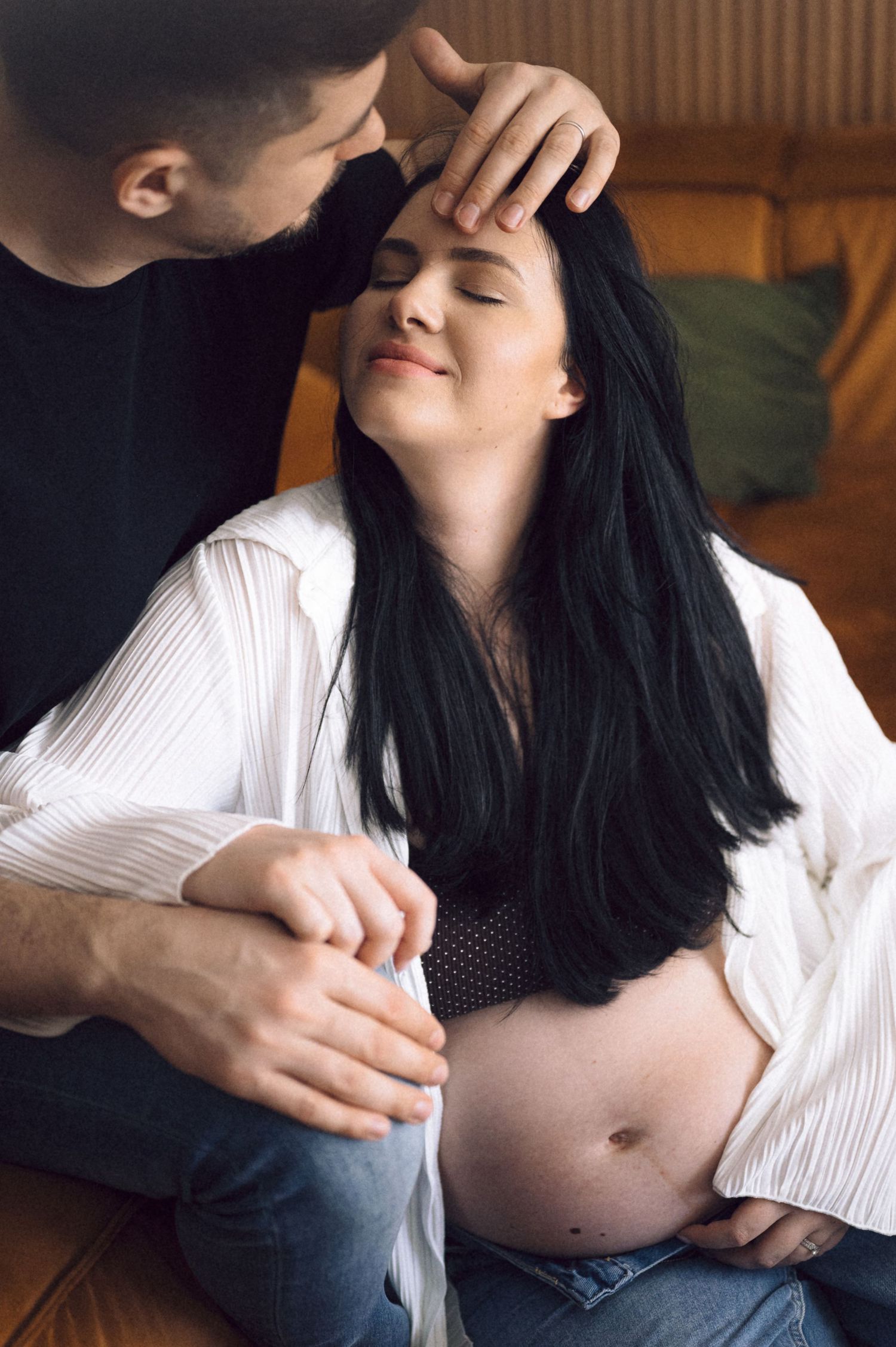 A series of intimate maternity photos showing a pregnant belly with hands gently resting on it in a white button down shirt.