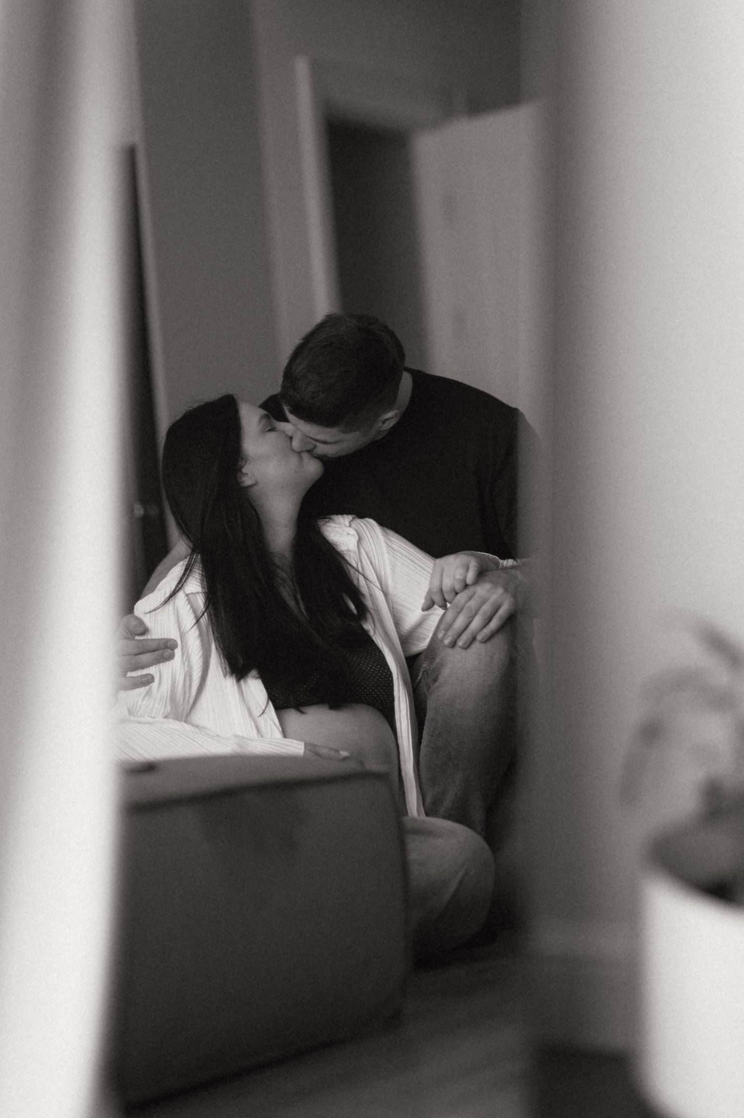 Black and white artistic photograph showing silhouettes of two people sitting on a couch in an intimate moment.