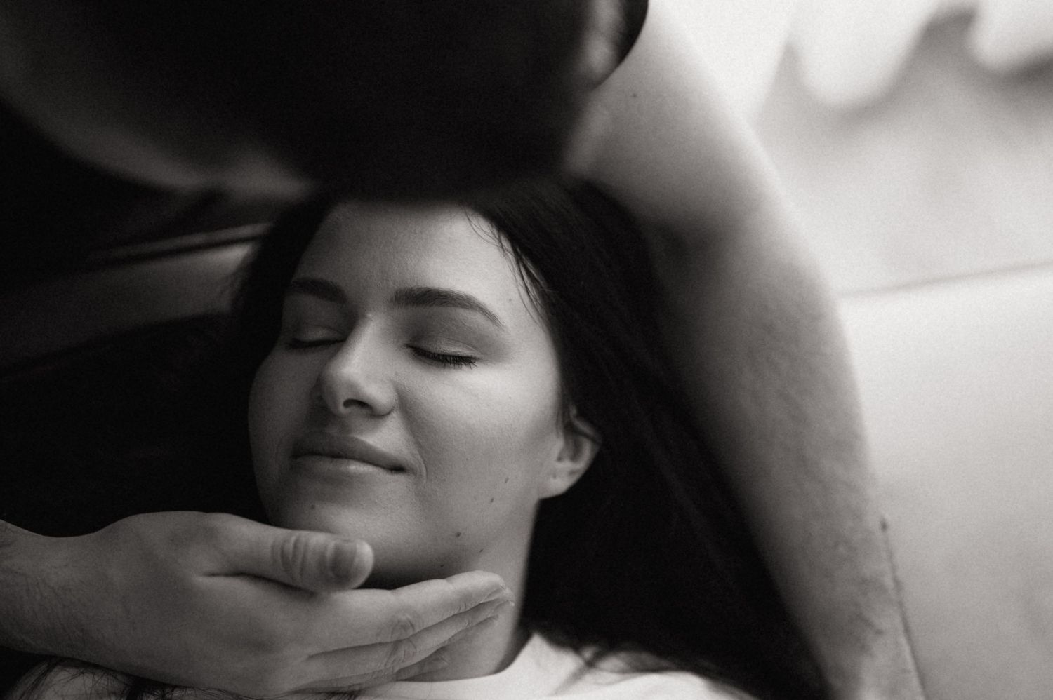 Black and white intimate portrait of person with eyes closed being tenderly touched on the face.