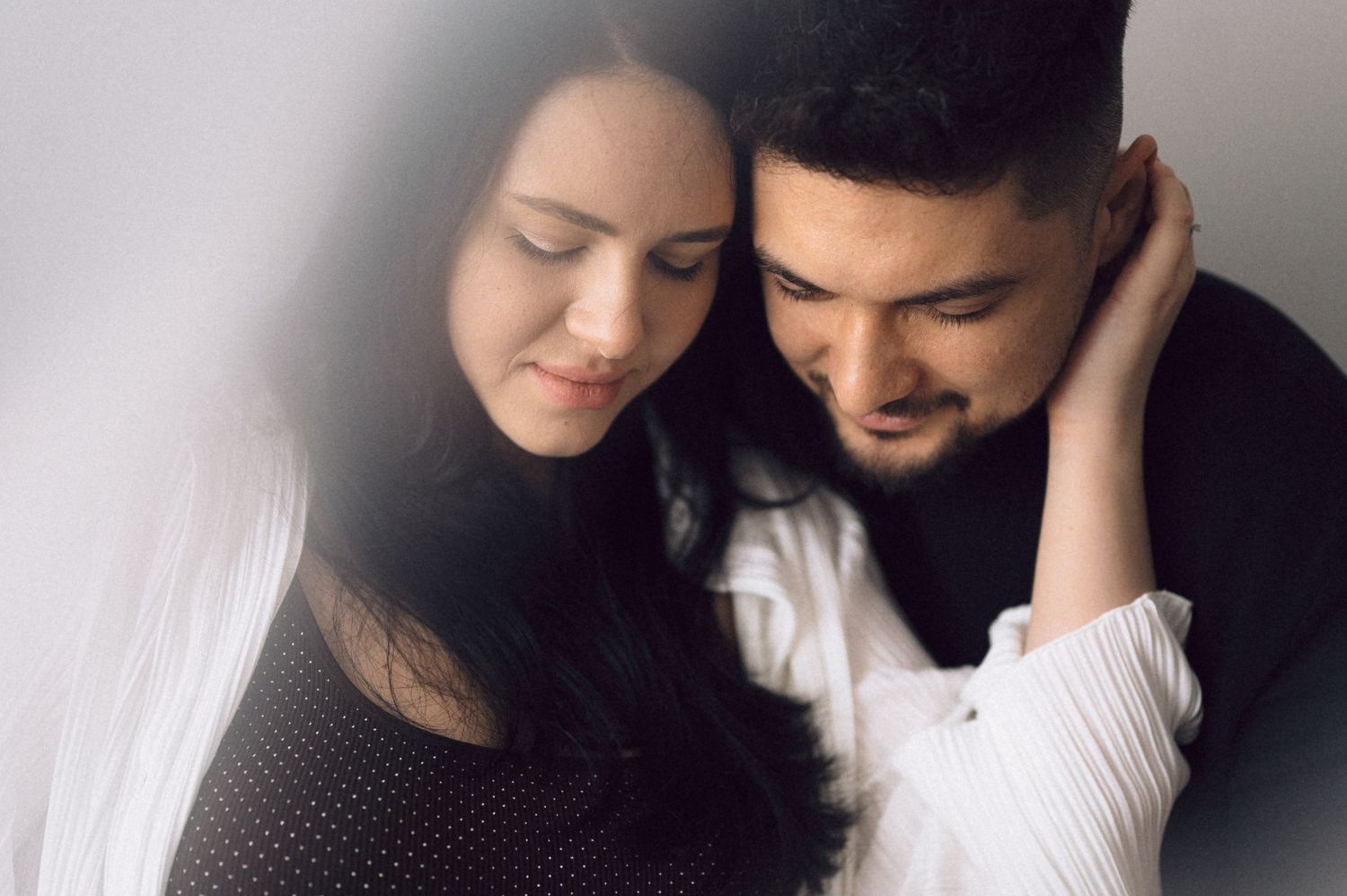An affectionate monochrome portrait of a couple sharing a gentle embrace in natural lighting.