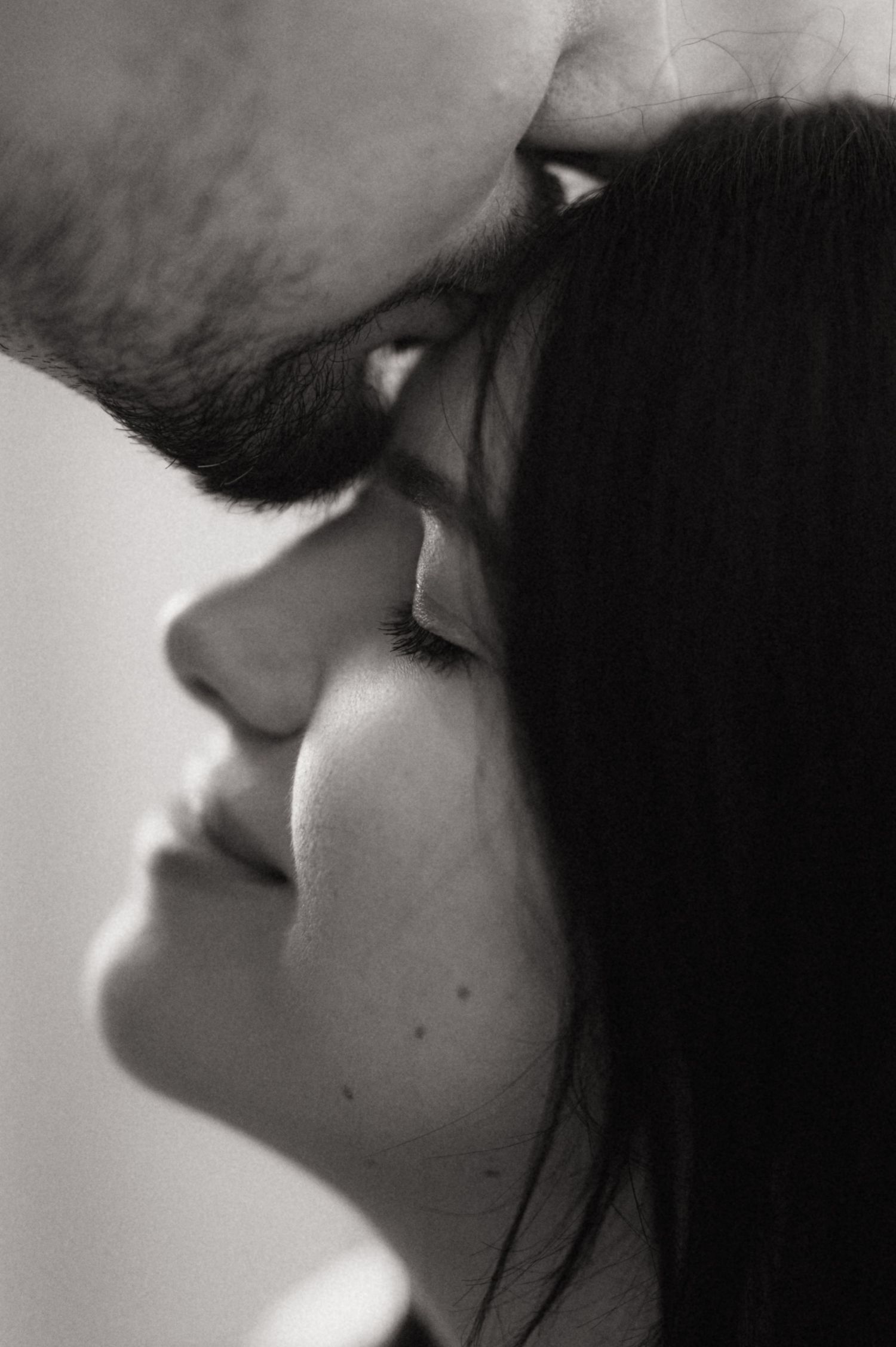 A black and white artistic profile portrait showing a tender intimate moment between two people in soft lighting.