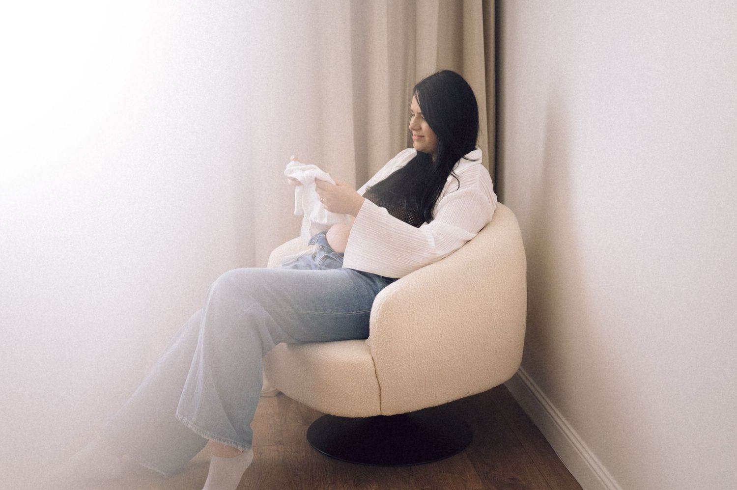 A black and white artistic photograph of a person resting in a white chair against a light wall.