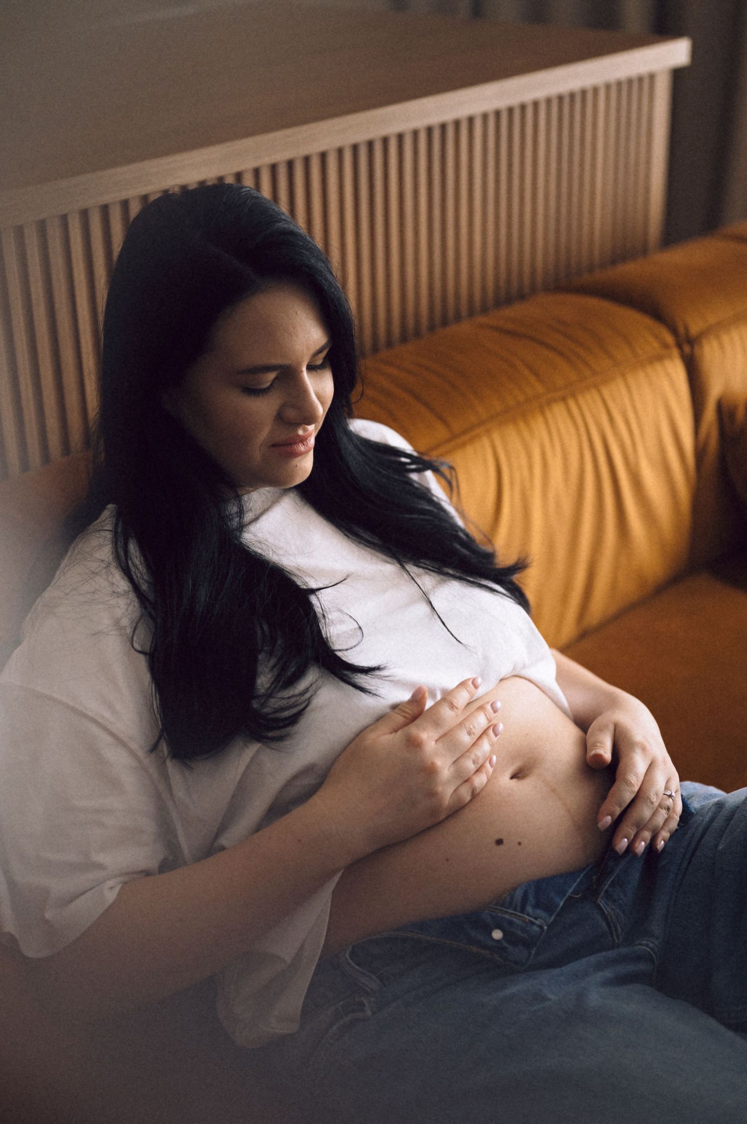 A series of intimate photos showing a pregnant woman's belly in soft lighting on a couch.