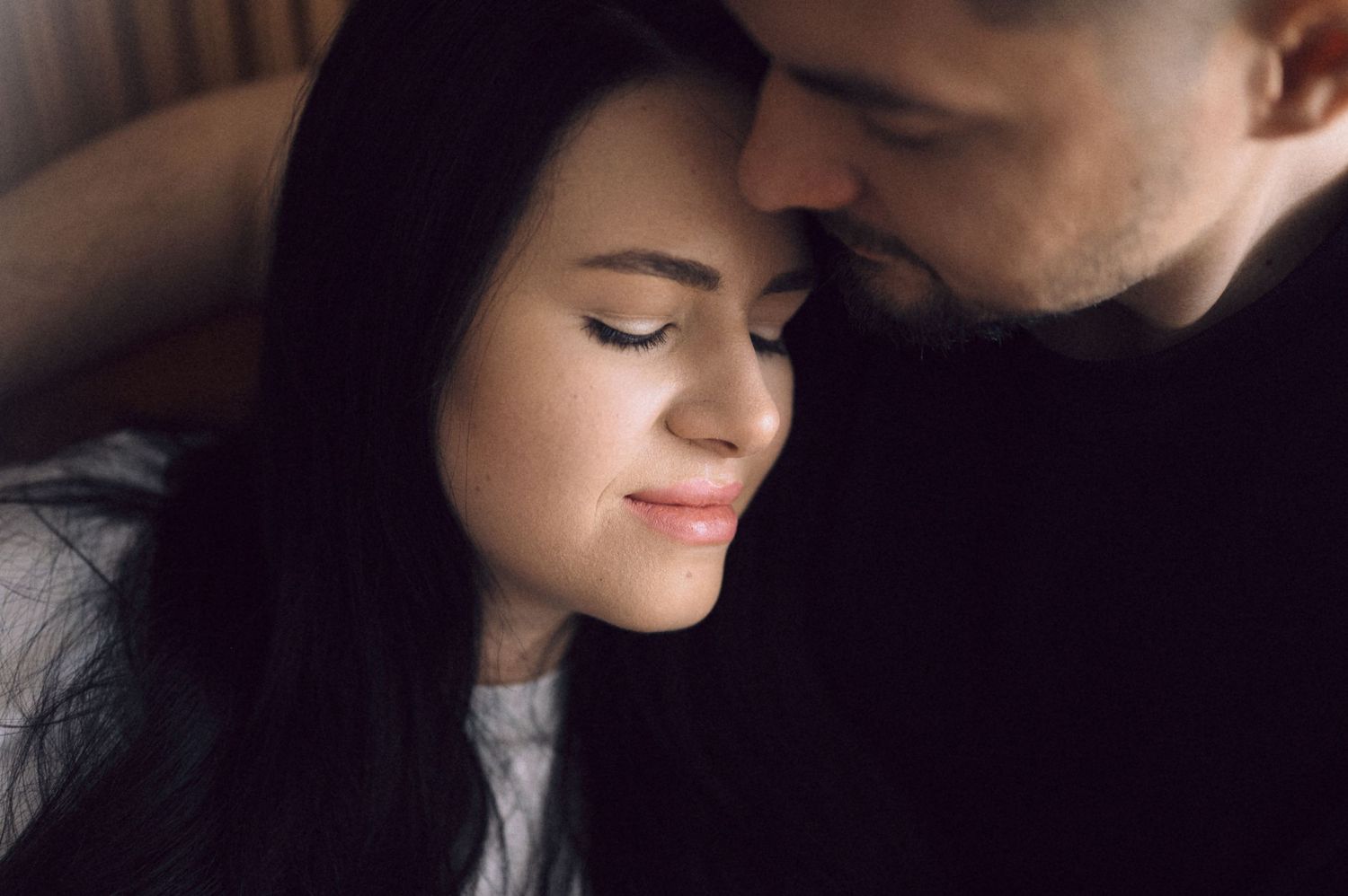 A tender intimate moment between a couple in soft lighting as they share a close embrace.