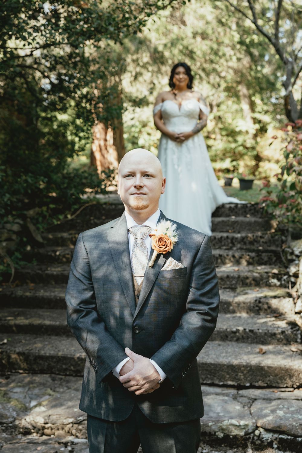 A wedding ceremony scene in a wooded outdoor setting with stone walls and natural lighting.