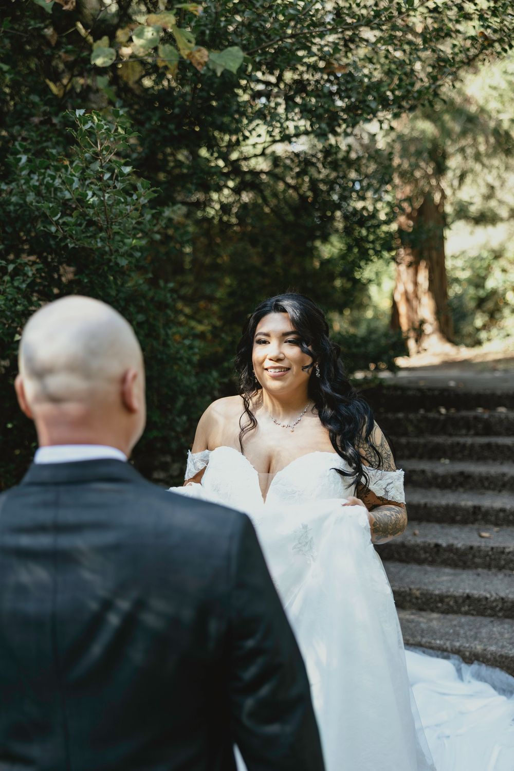 A bride in a white wedding dress walks up stone steps in a wooded outdoor setting.