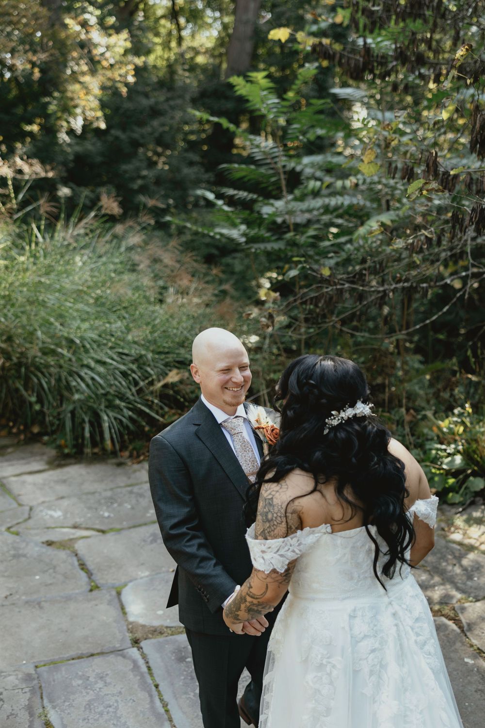 A couple shares a romantic moment on their wedding day in a lush garden setting with stone pathways.