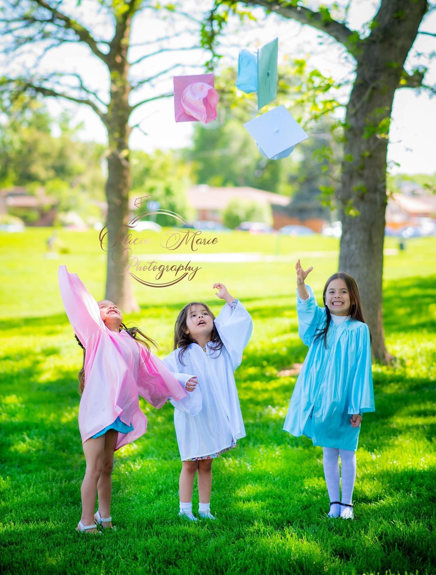 Three children in colorful dresses playing with graduation caps outdoors on a spring day.