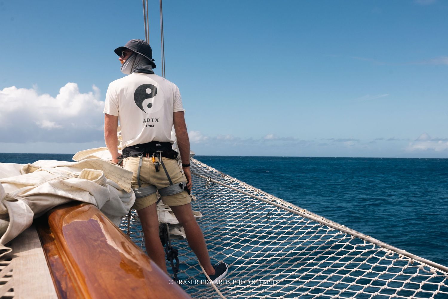 People relaxing on a catamaran's mesh netting while sailing across bright blue tropical waters on a sunny day.