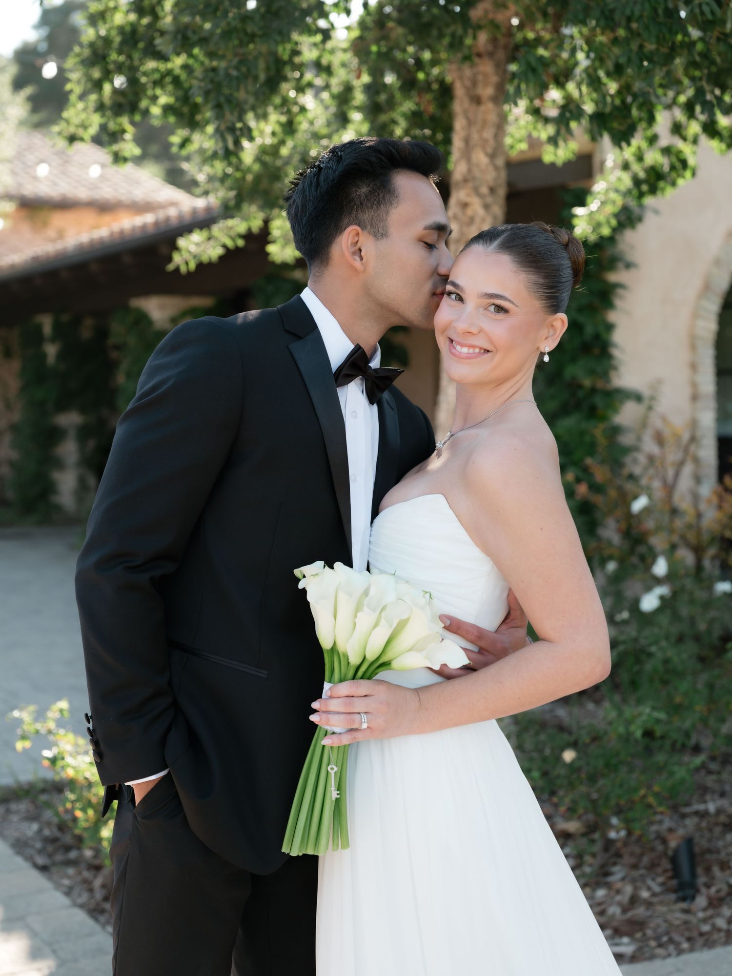A bride and groom share intimate moments in a garden setting with natural lighting and white calla lily bouquet.