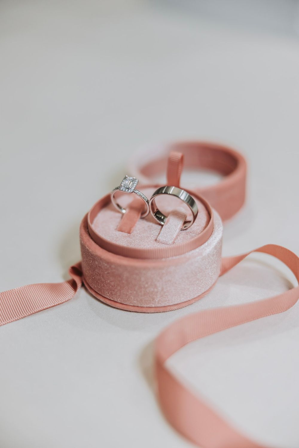 Two silver wedding rings displayed in an open pink velvet ring box with ribbon on a white background.