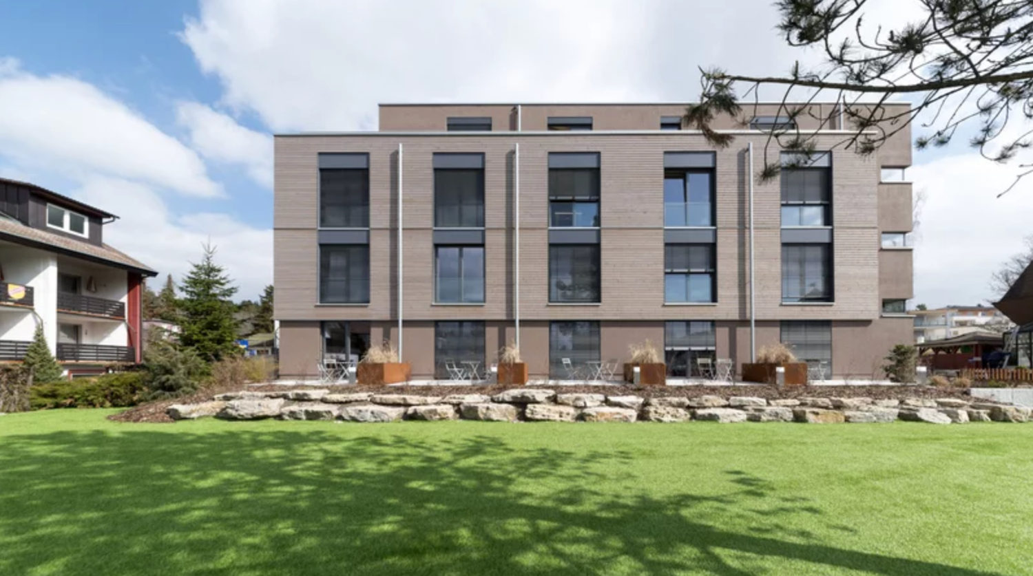 Modern apartment buildings with glass facades and balconies surrounded by landscaped grounds and trees.