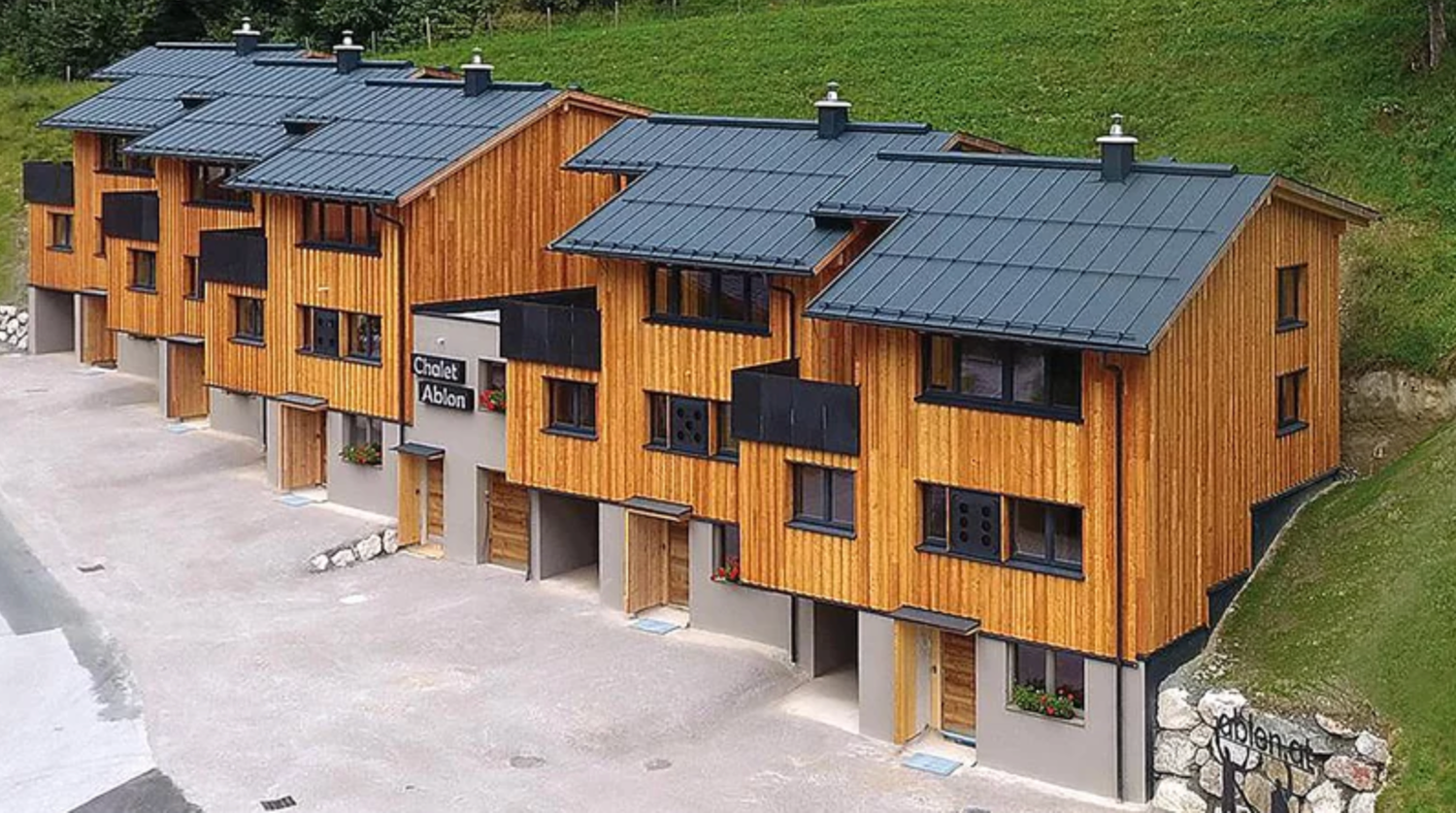 Modern wooden apartment complex with solar panels on sloped roofs nestled in a green hillside setting.