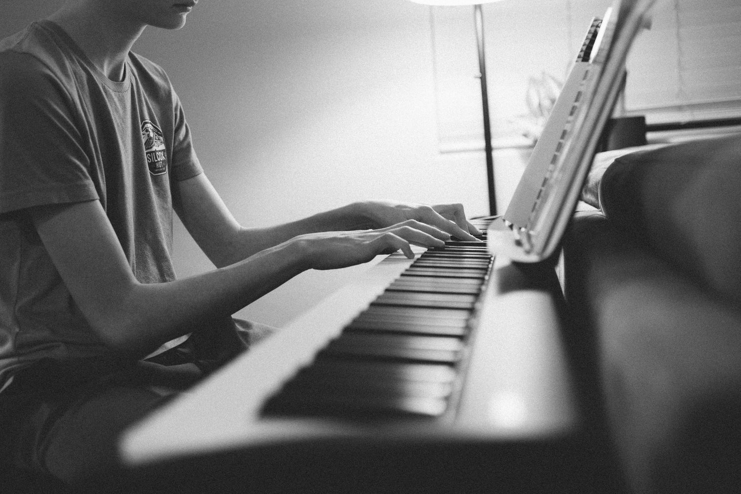 Black and white close-up of teenager playing piano with sheet music in background.