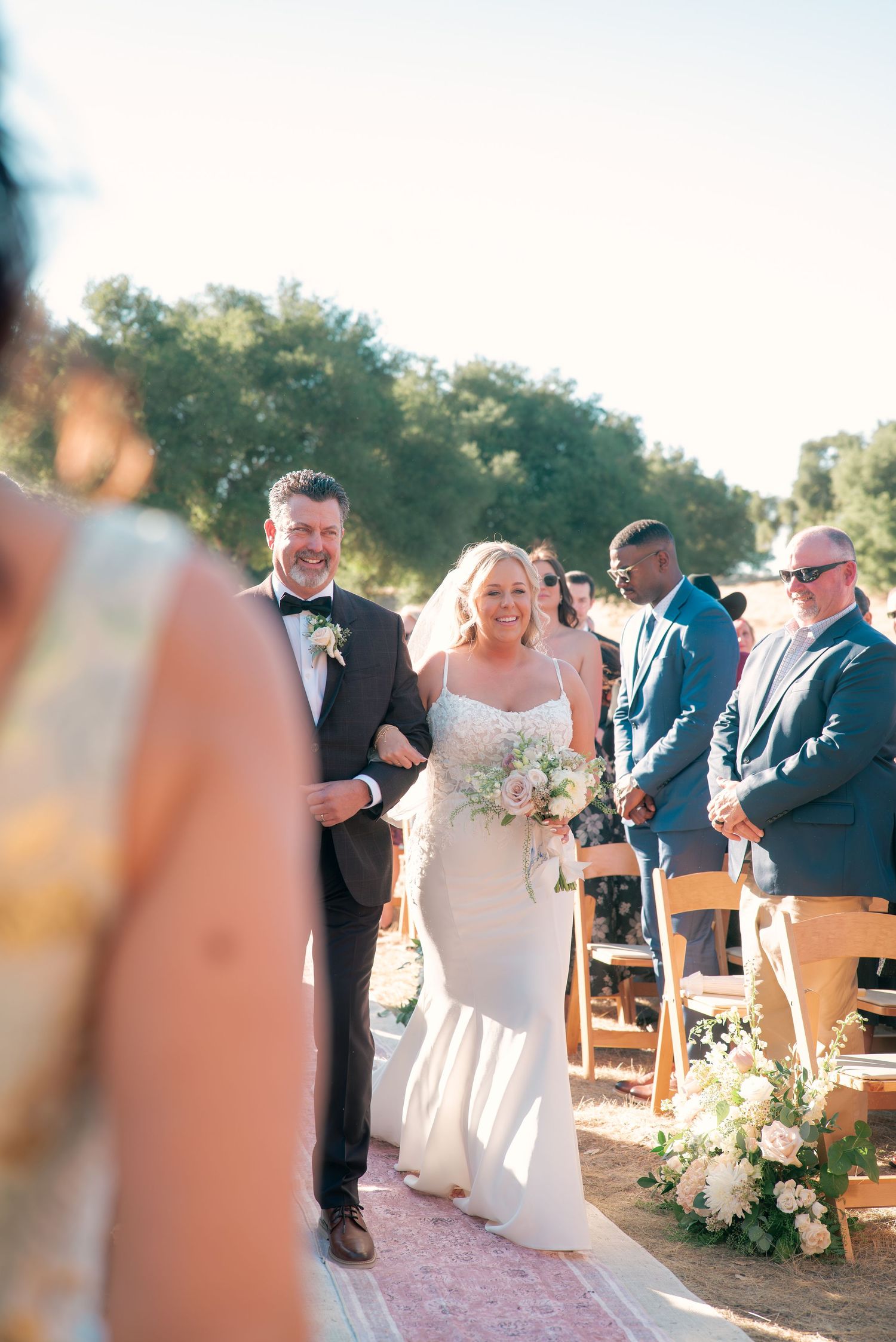 Outdoor wedding ceremony setup with wooden chairs and floral arrangements at sunset.