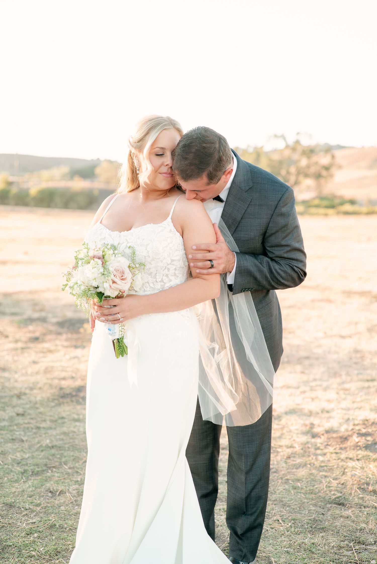 Romantic wedding couple embracing in a golden sunset field during their photo session.