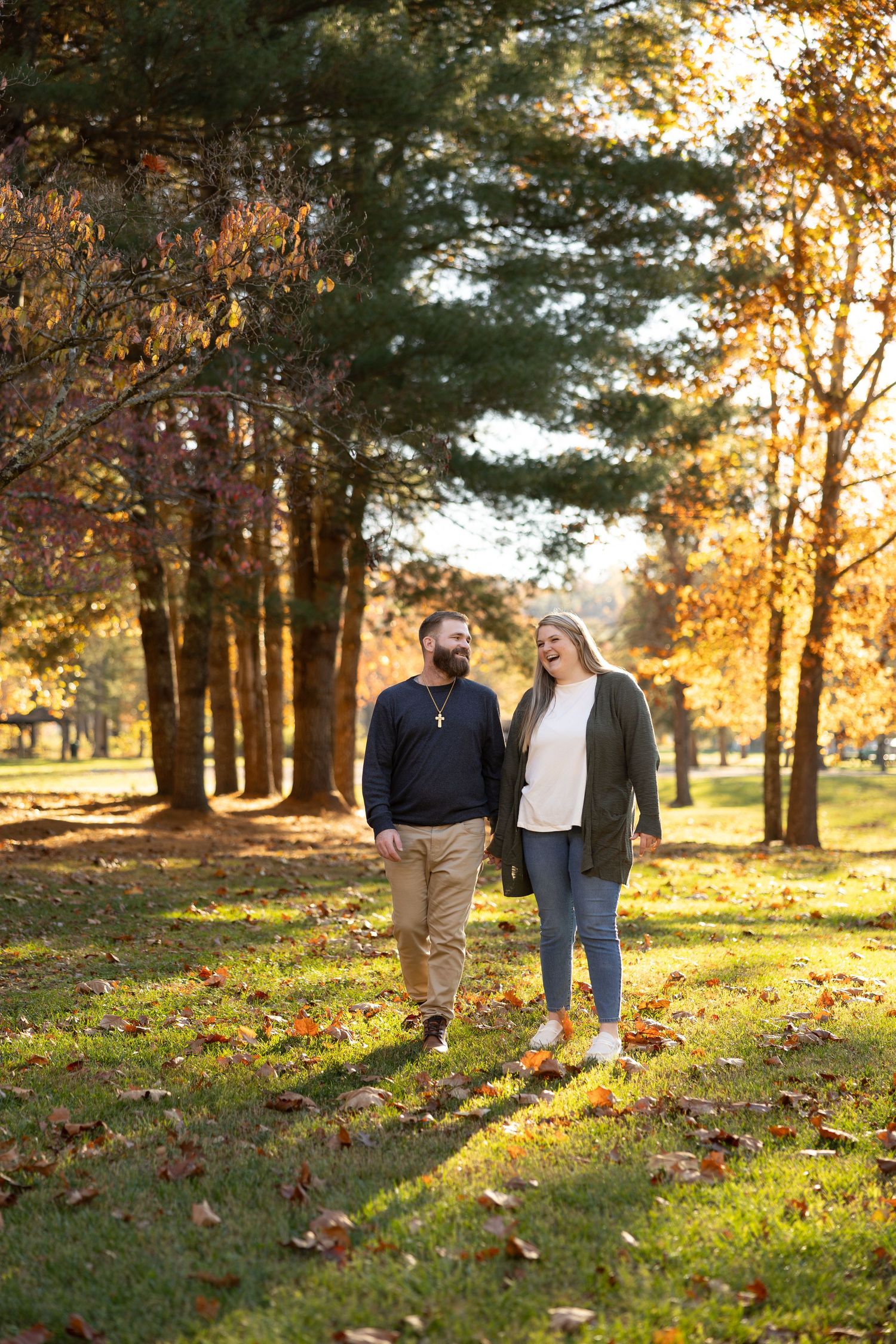 A couple shares a romantic kiss under tall pine trees during golden hour in an autumn setting.