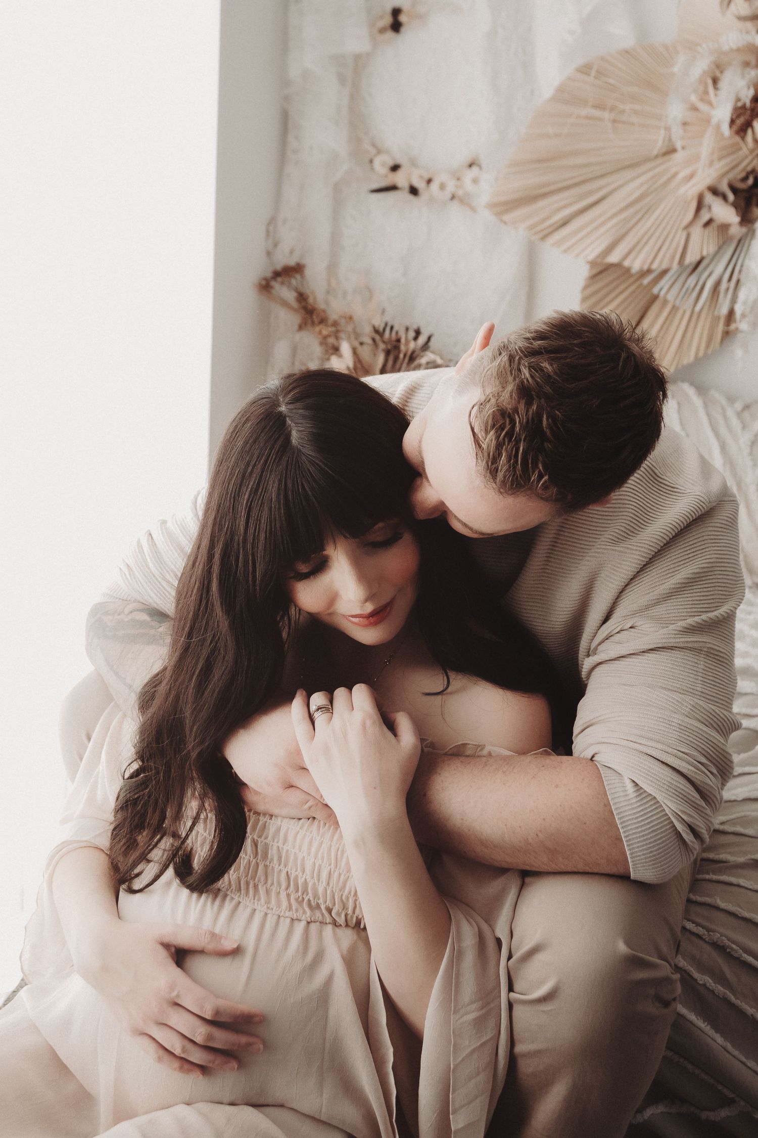 Intimate couple lying together in bed with soft beige tones and natural light creating a romantic atmosphere.