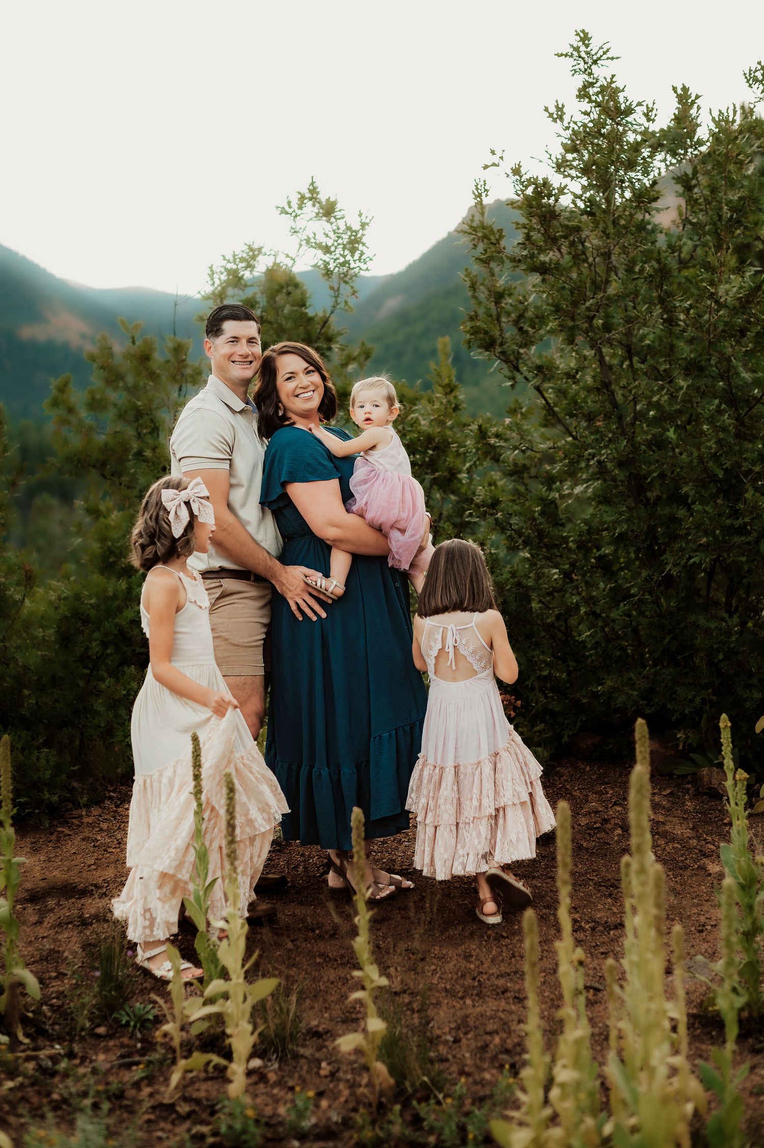 Family wearing coordinated outfits poses together against mountain backdrop with desert plants at sunset.