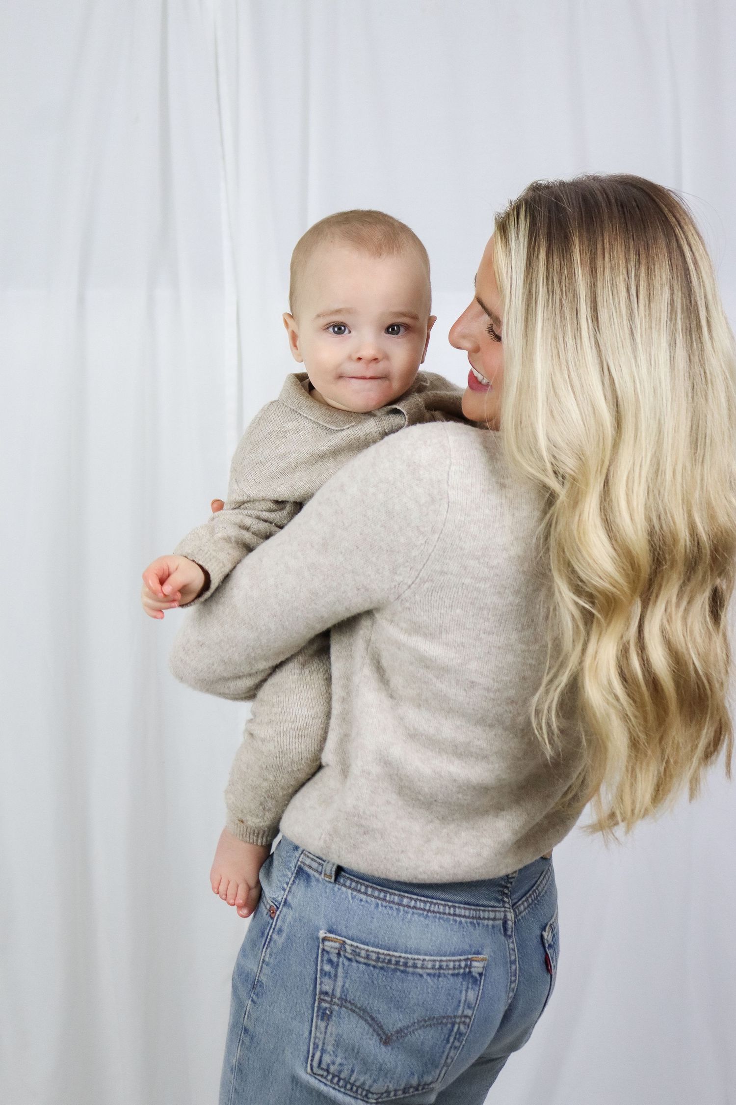 A parent and baby wearing matching gray sweaters share tender moments together against a white backdrop.