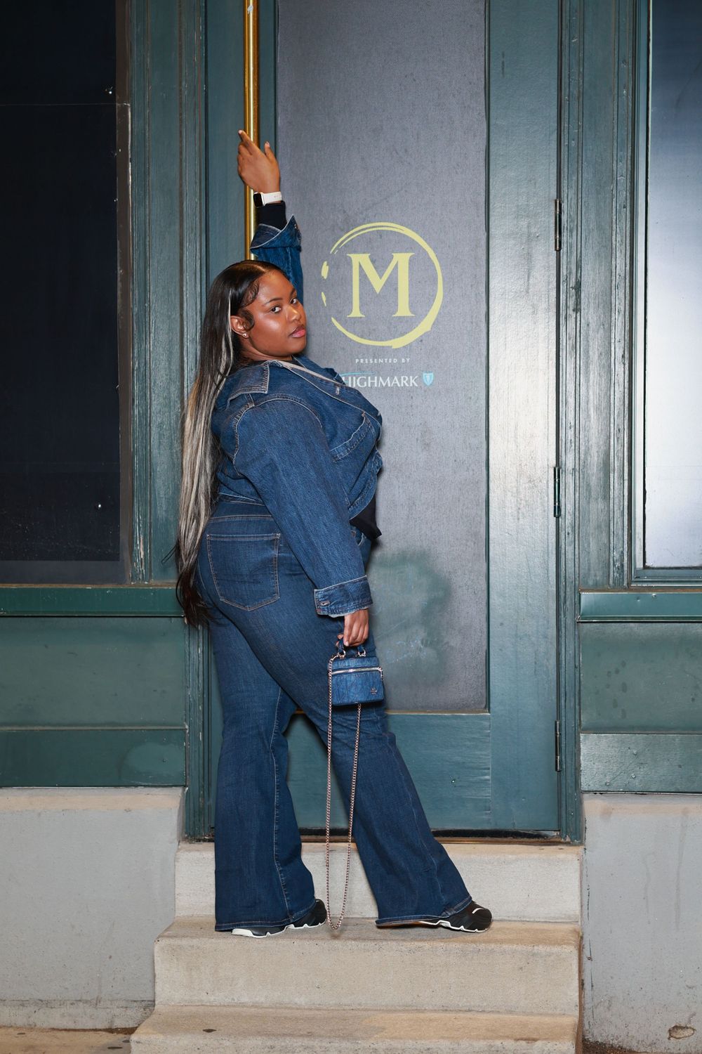 Person in denim overalls reaches for a door handle at night while standing on concrete steps.