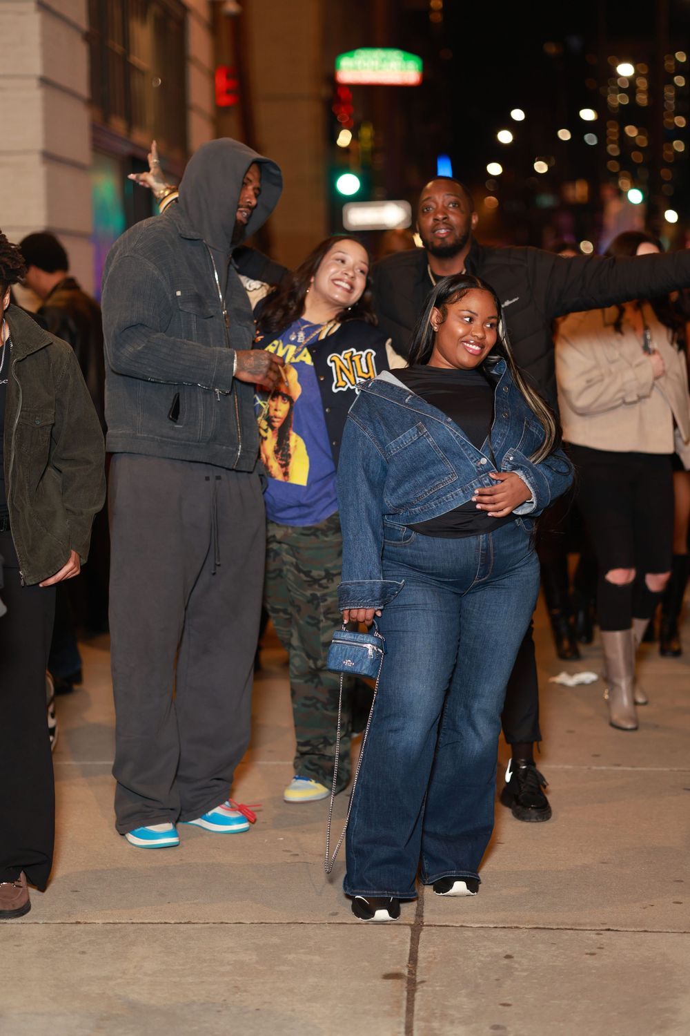 Two people share a playful moment on a city sidewalk at night while holding snacks and drinks.