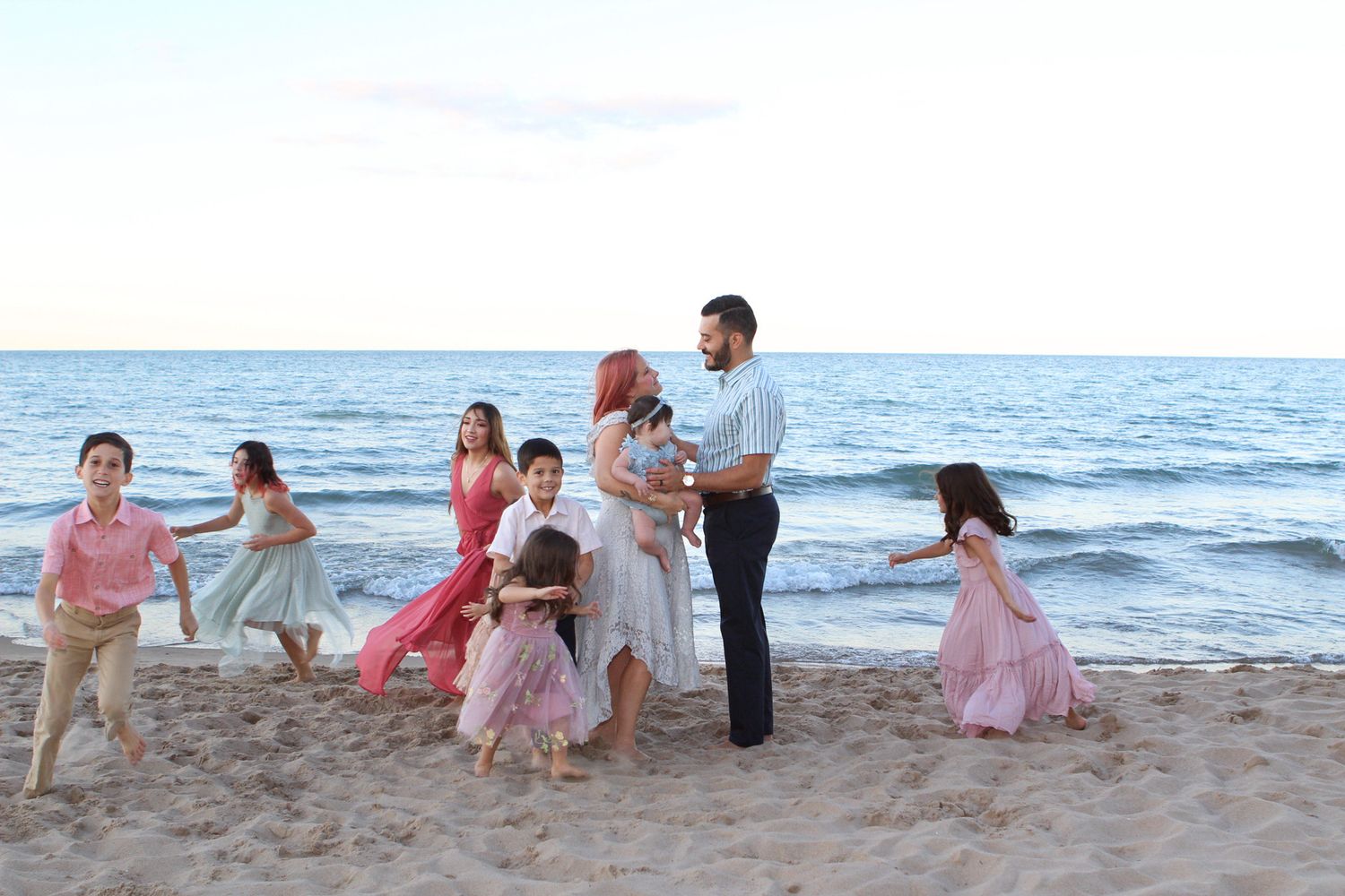 Family group poses together on a sandy beach at sunset while wearing coordinated pink and white outfits.