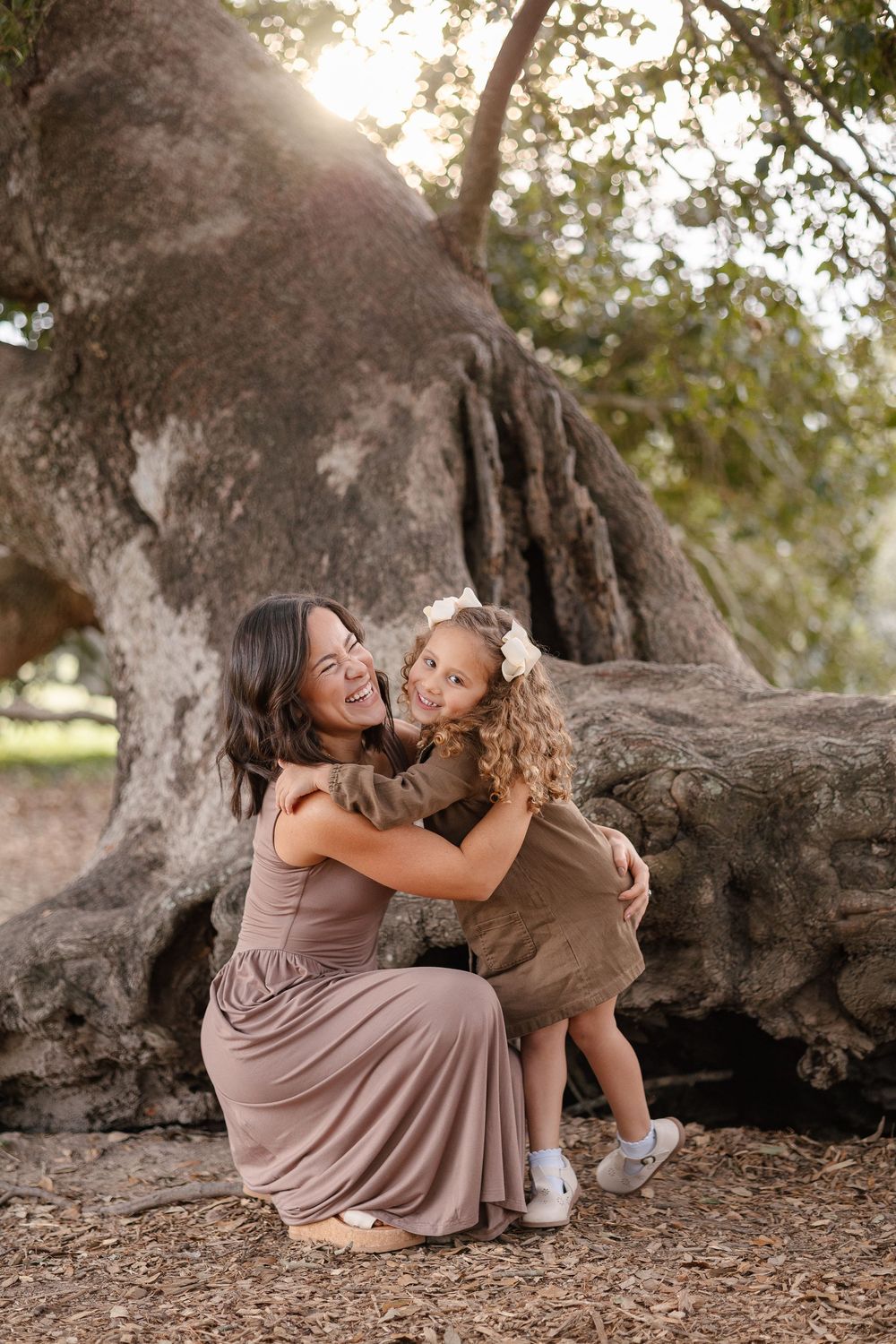 A touching moment between parent and child sitting together under a large tree at sunset.