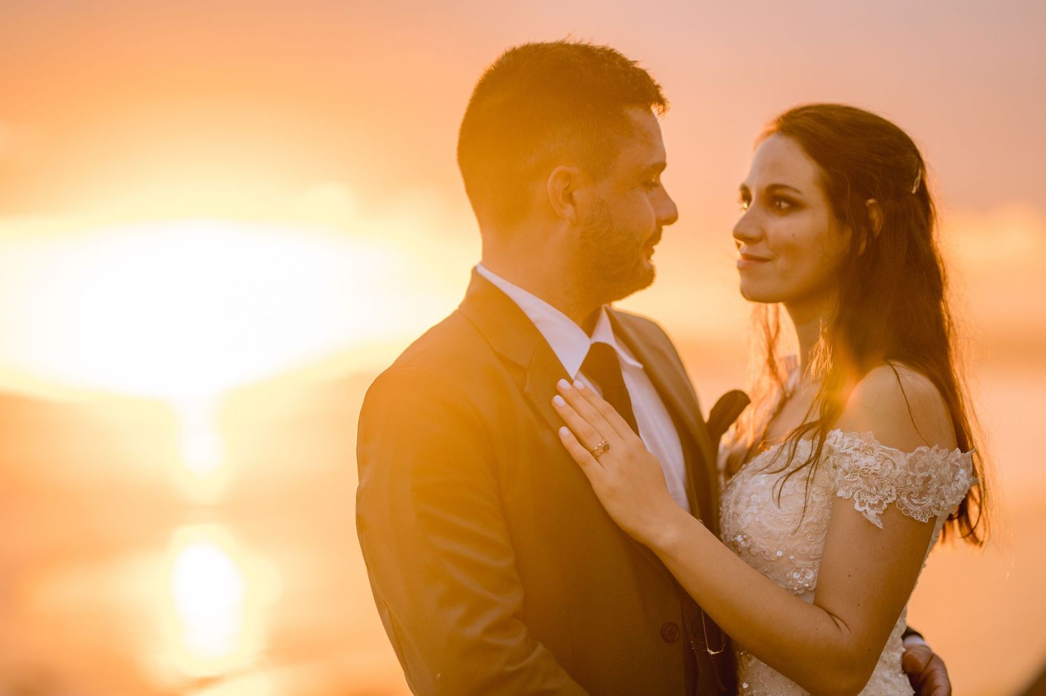 A romantic couple embraces during a golden sunset photoshoot with a warm glowing sky in the background.
