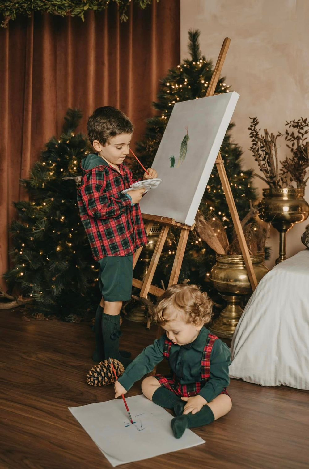 Two children creating art at Christmas time with an easel and drawing supplies.