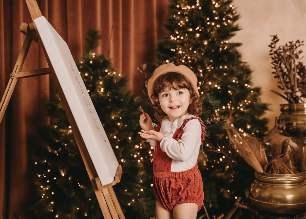 A charming holiday scene with an art easel and Christmas tree in the background with warm lighting.