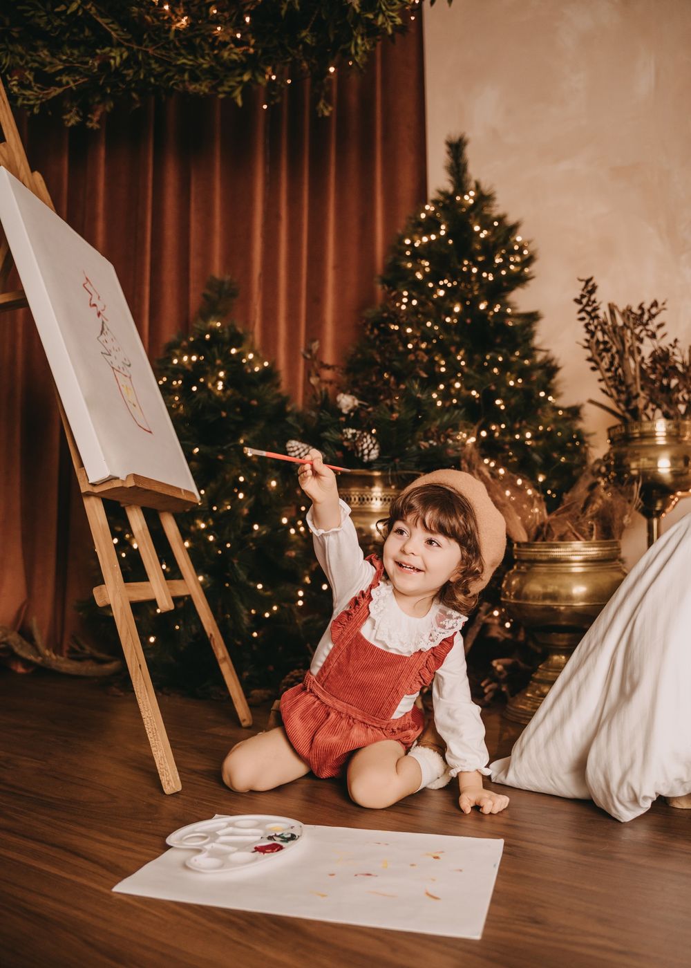 A whimsical art scene with an easel, drawings, and Christmas decorations in a warmly lit room.