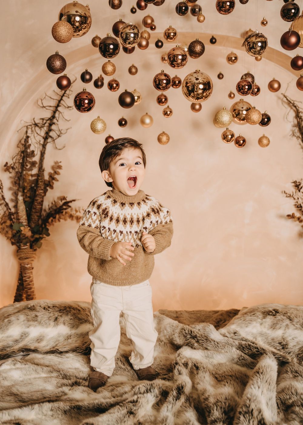 A festive holiday scene with floating gold ornaments and a Fair Isle sweater against a neutral background.