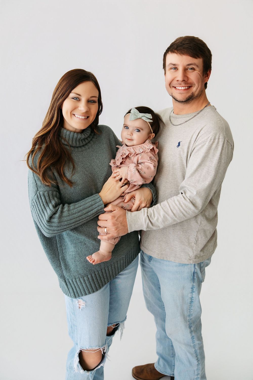 Happy family in coordinating teal and gray outfits pose together against white background in lifestyle photoshoot.