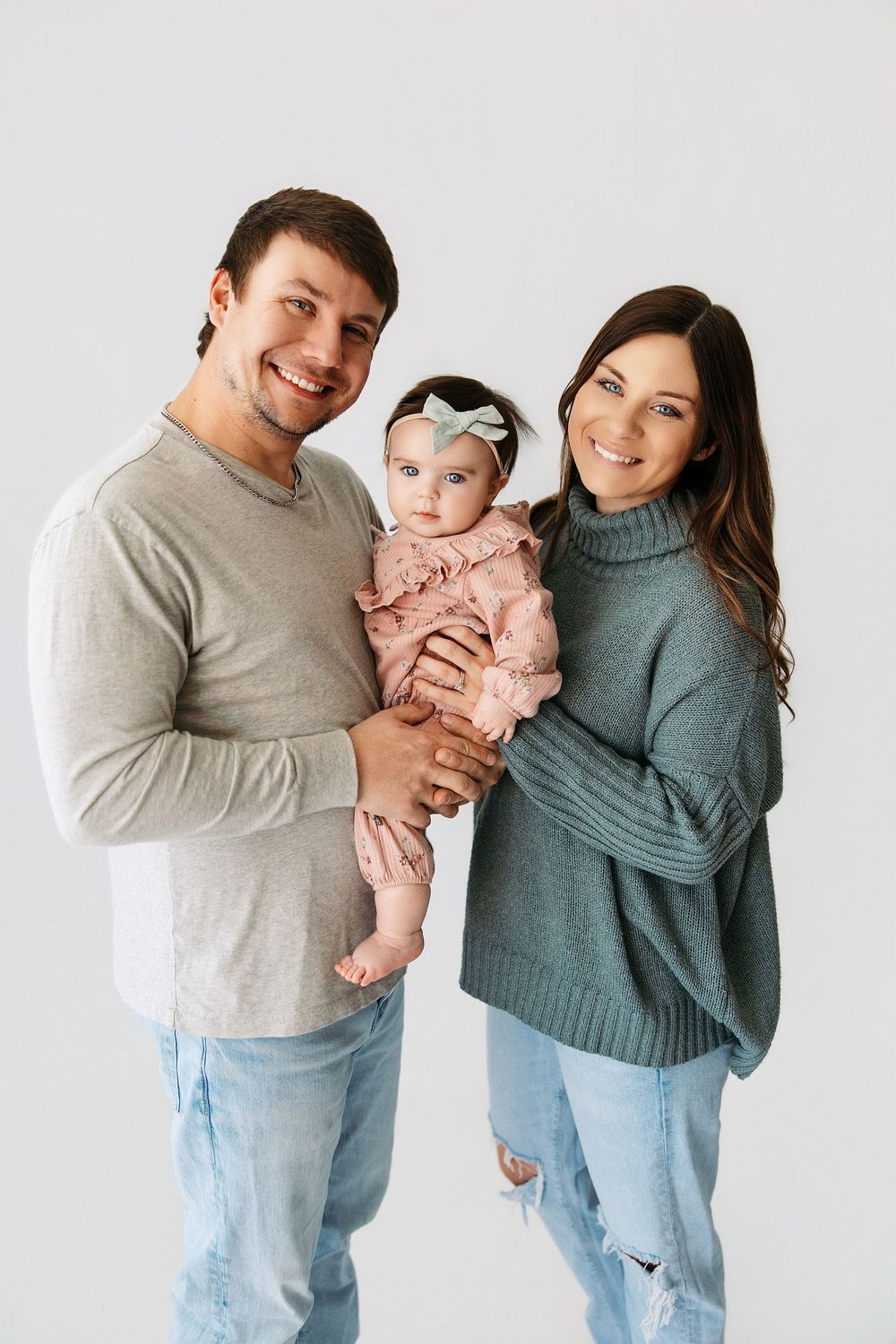A family poses together against a white background wearing casual sweaters and jeans.
