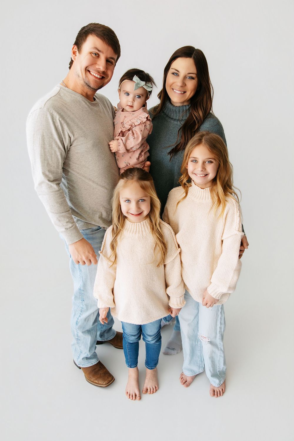 A family in coordinated casual outfits of light denim and neutrals poses together against a white backdrop.