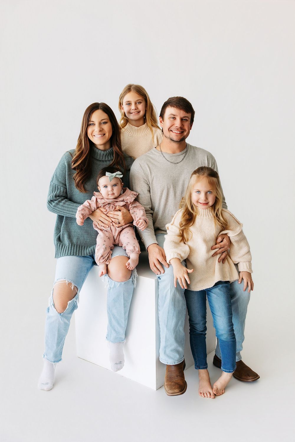 Family in coordinated casual outfits sitting together on white background in studio portraits.