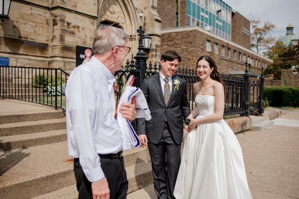 A wedding party shares a joyful moment together on stone steps outside a historic building.