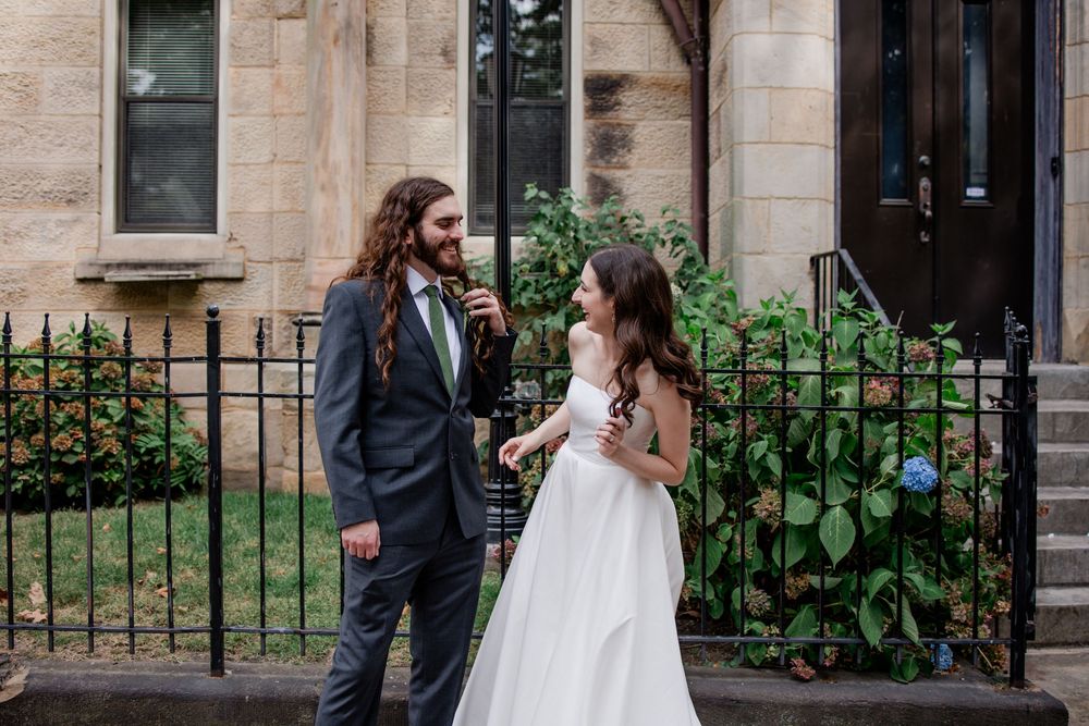 A bride and groom share a candid moment together outside a stone building with an ornate iron fence.