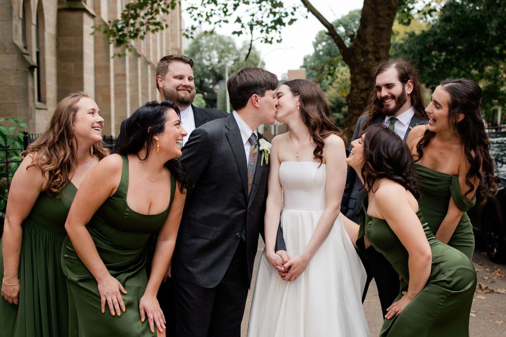 Wedding party in olive green and white dresses poses together outdoors in a garden setting.