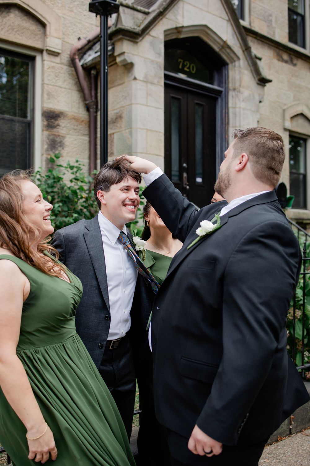 A joyful moment shared between wedding party members in formal attire outside a brick building entrance.