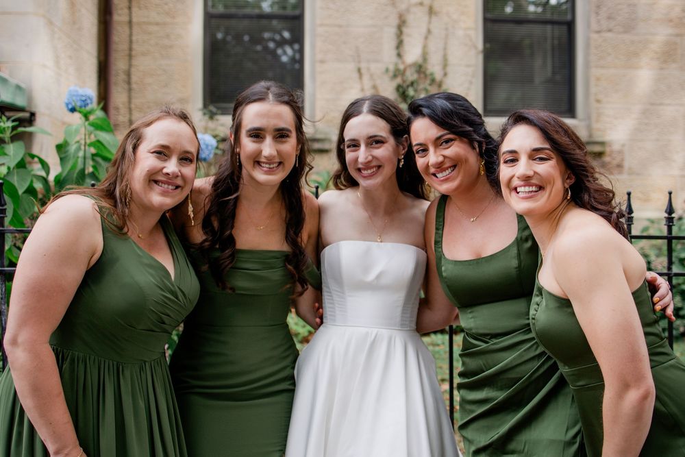 A wedding party poses together wearing olive green bridesmaid dresses and a white wedding gown.