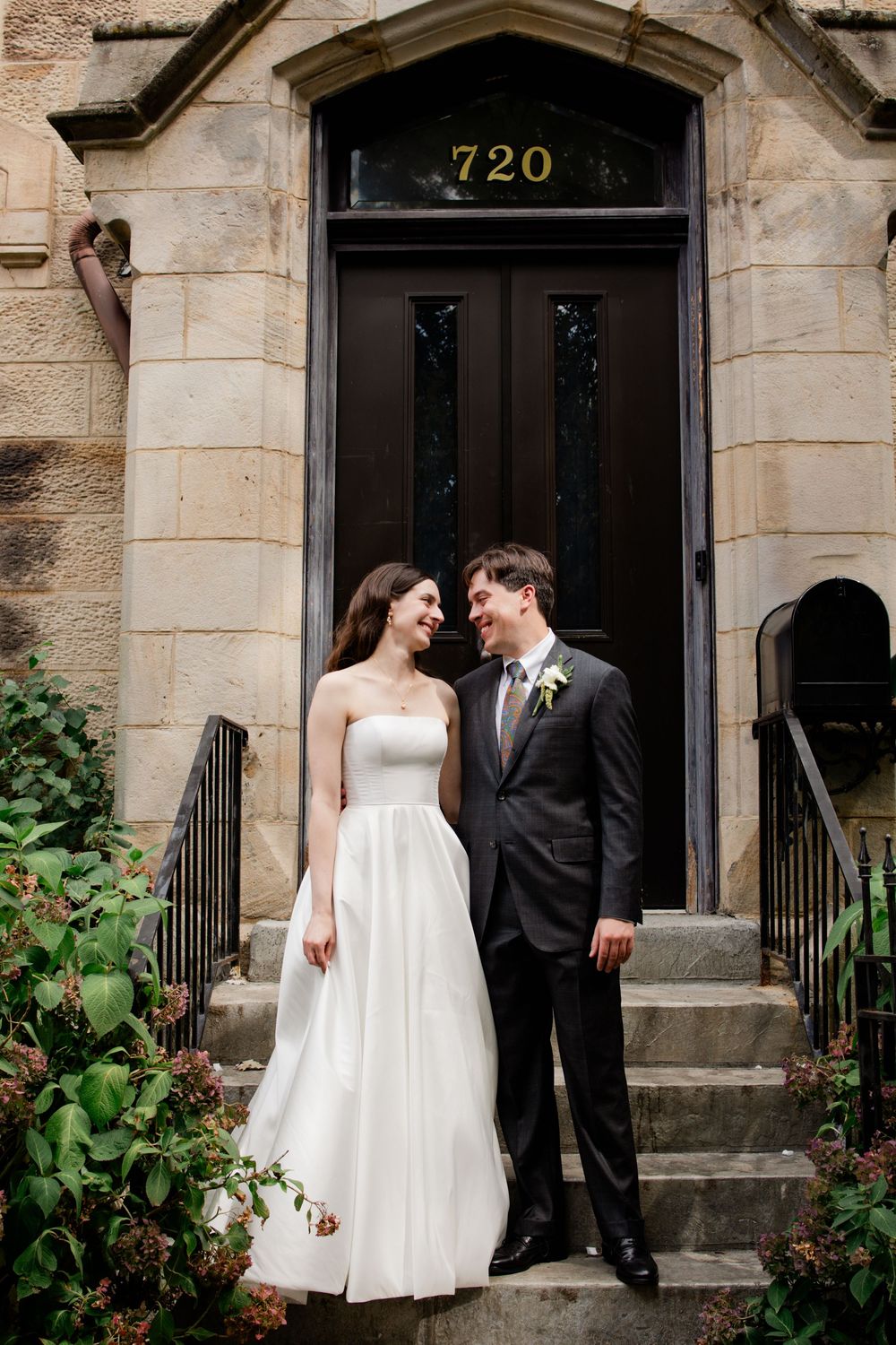 A romantic wedding couple poses together in front of a historic stone building entrance with black doors.