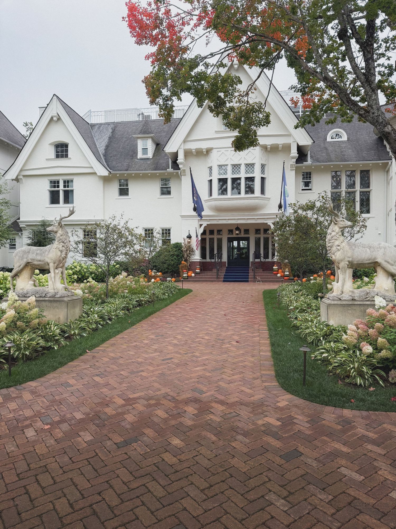 Curved brick walkway leading to white Victorian-style houses with autumn trees and landscaped gardens.