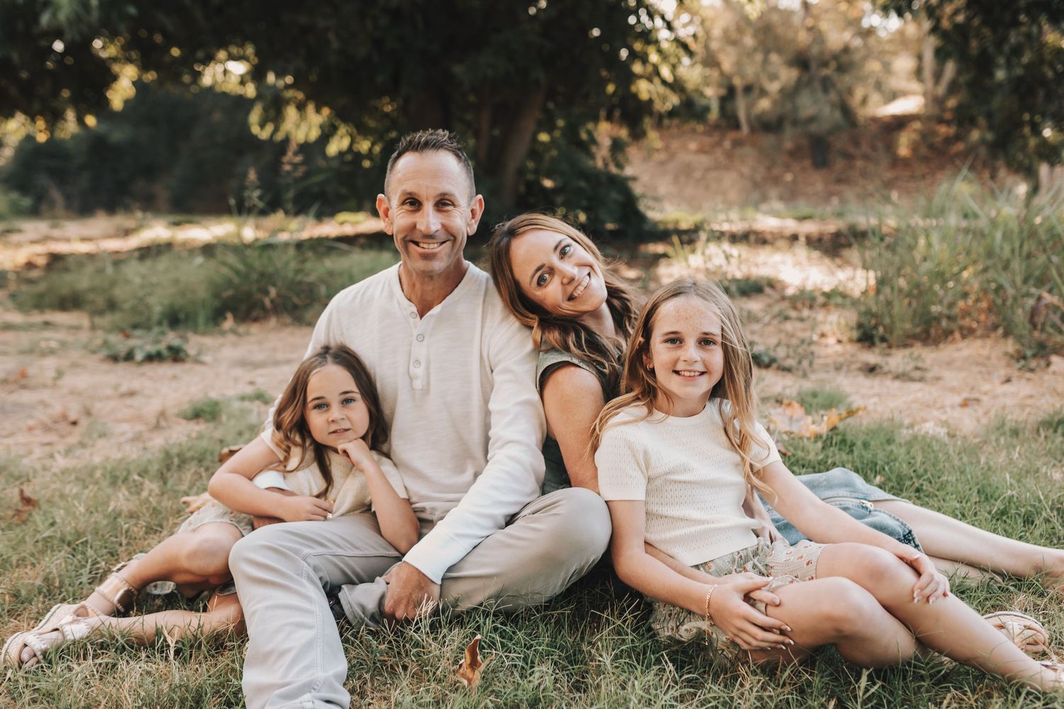 A family sits together on grass during a casual outdoor photo session at sunset.
