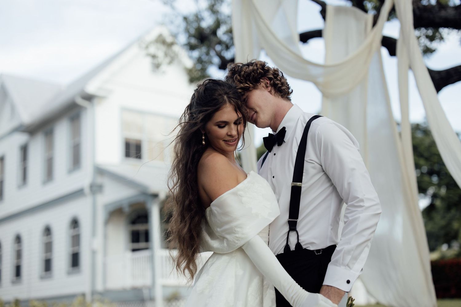 A couple embraces during a romantic outdoor wedding photoshoot with white buildings in the background.