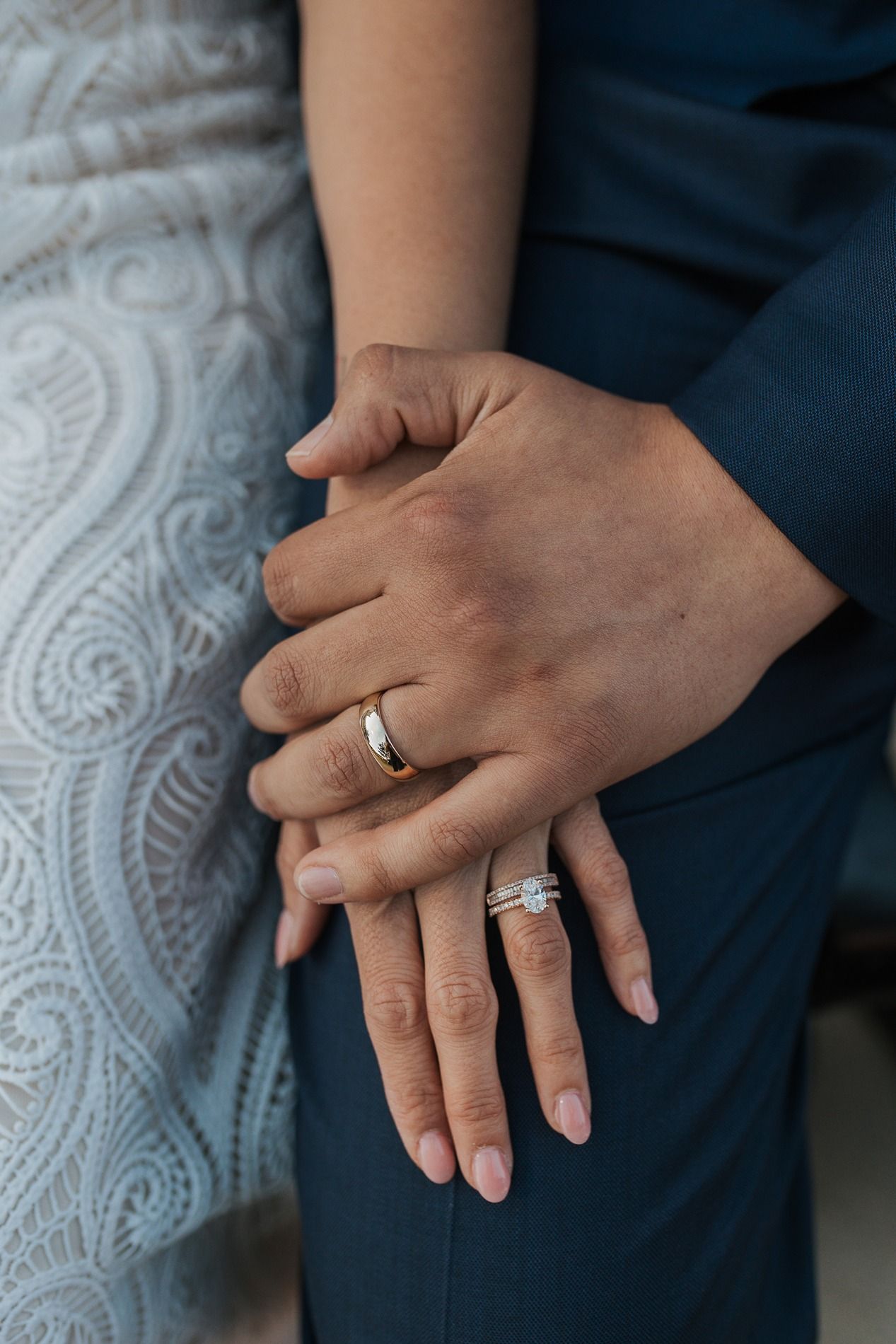 Close-up of hands wearing engagement and wedding rings against a backdrop of paisley fabric and dark clothing.